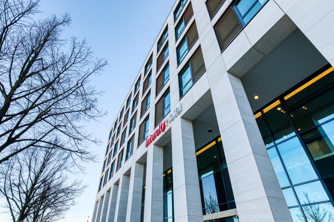 Intercityhotel Berlin Airport Ber Terminal 1 & 2 Schonefeld Bagian luar foto The photo shows a modern building with a sleek, contemporary design. The structure features several large windows and a façade composed of light-colored stone. There is a visible entrance with glass doors, and the building appears to be several stori