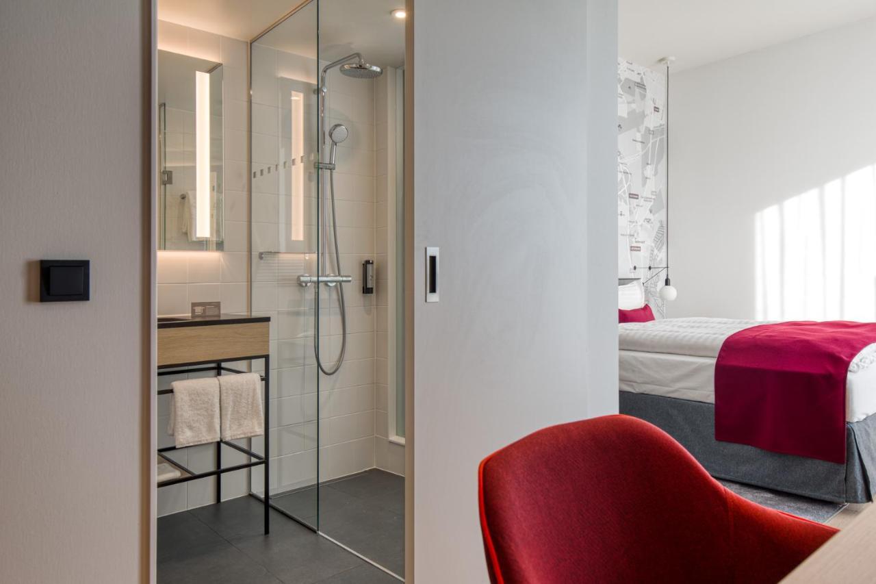 Intercityhotel Berlin Airport Ber Terminal 1 & 2 Schonefeld Bagian luar foto The photo shows a modern hotel room or bathroom space. On the left, there is a glass-enclosed shower area with a sleek design, featuring a showerhead and minimalist fixtures. Adjacent to the shower, there's a sink area with a stylish countertop and a